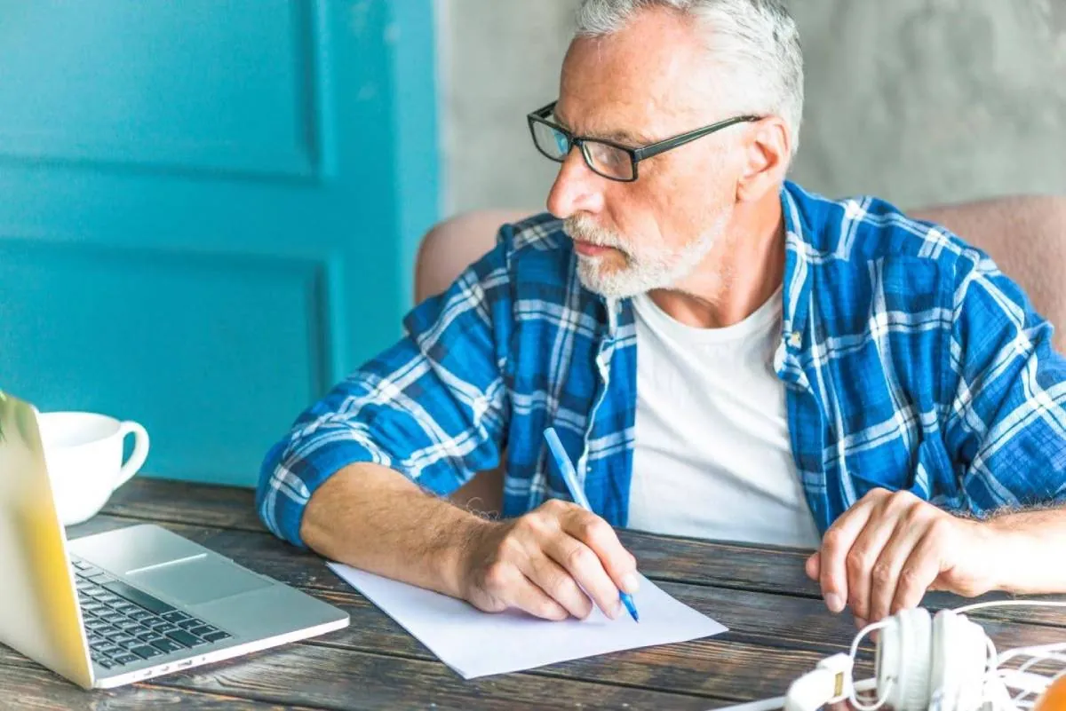 An older woman who is working at her computer writing down family caregiver time management tips.